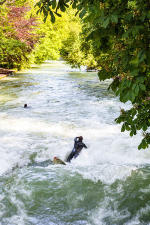 MUNICH, GERMANY - MAY 22, 2018: people surfing at urban stream Eisbachwelle in Munich city. Munich is the capital city and the most populated city in the German state of Bavariaのeditorial素材