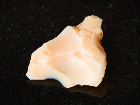 macro shooting of natural mineral - rough noble opal gemstone on black granite from Ural Mountains