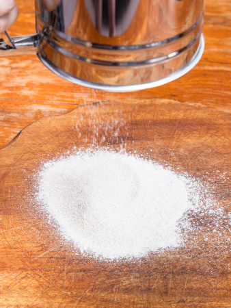 cooking of pie - flour pouring through sifter on wooden boardの写真素材