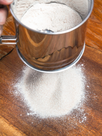 cooking of pie - sifting the flour through steel sieve on wooden boardの写真素材