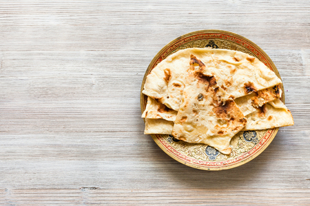 Indian cuisine - Naan flat bread baked in tandoor on brass plate on gray wooden tableの写真素材