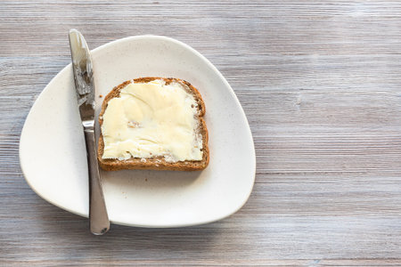 top view of bread sandwich with buttered butter and steel knife on white plate on gray wooden board...