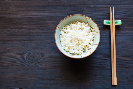 top view of portion of boiled rice in cup and chopsticks on rest on dark table with copyspaceの写真素材