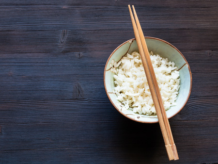 top view of chopsticks above cup with boiled rice on dark brown table with copyspaceの写真素材