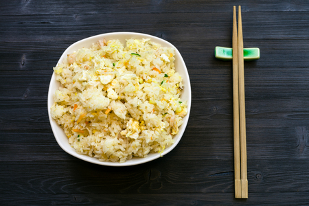 Chinese cuisine dish - top view of served portion of Fried Rice with Shrimps, Vegetables and Eggs (Yangzhou rice) with chopsticks on dark wooden tableの写真素材