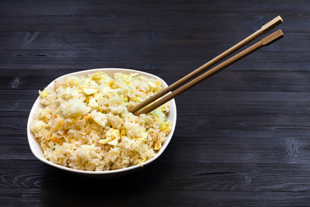 Chinese cuisine dish - bowl with Fried Rice with Shrimps, Vegetables and Eggs (Yangzhou rice) with chopsticks on dark wooden tableの写真素材