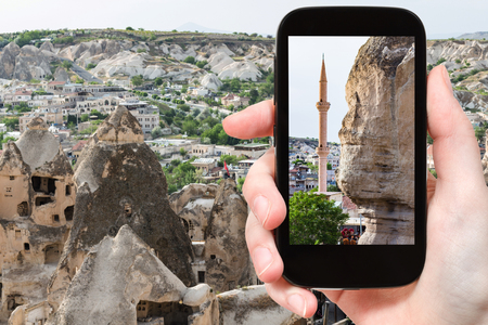 travel concept - tourist photographs of wall of ancient rock-cut house and mosque in Goreme town in Cappadocia on smartphone in Turkey in springの写真素材