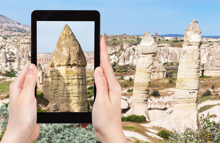 travel concept - tourist photographs of landscape with old fairy chimney rocks in mountains of Goreme National Park in Cappadocia on smartphone in Turkey in springの写真素材