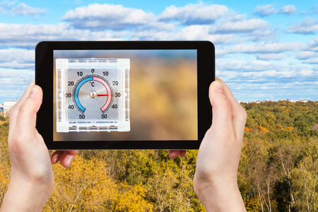 travel concept - tourist photographs city park and outdoor thermometer on home window in hot autumn day on smartphone in Moscow, Russiaの写真素材