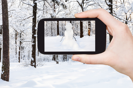 travel concept - tourist photographs of snowman at snowy meadow in winter morning on smartphone in Moscow, Russiaの写真素材