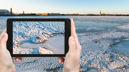 travel concept - tourist photographs of ice-bound Neva river near Dvortsovaya Embankment in Saint Petersburg city in Russia on smartphone in springの写真素材