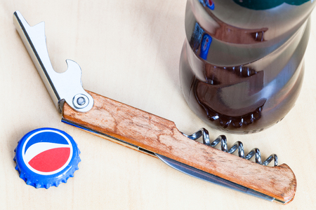 MOSCOW, RUSSIA - APRIL 4, 2019: used crown cap and bottle opener near Pepsi glass bottle on wooden board close up. Pepsi is carbonated soft drink manufactured by PepsiCoのeditorial素材