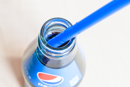 MOSCOW, RUSSIA - APRIL 4, 2019: above view of open glass bottle of Pepsi beverage with blue drinking straw close up. Pepsi is carbonated soft drink manufactured by PepsiCoのeditorial素材