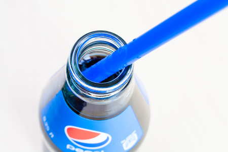 MOSCOW, RUSSIA - APRIL 4, 2019: top view of open glass bottle of Pepsi beverage with blue drinking tube close up. Pepsi is carbonated soft drink manufactured by PepsiCoのeditorial素材