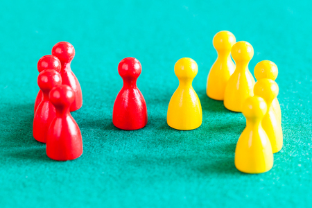 concept scene - few red pawns with leader in front of several yellow pawns with leader on green baize tableの写真素材