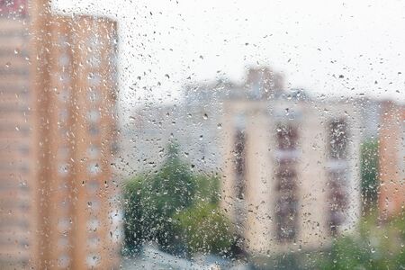 Raindrops on home window glass and blurred cityscapeの写真素材
