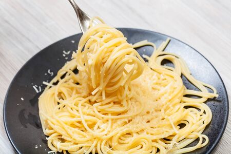 fork wrapped by spaghetti al burro e parmigiano (pasta with butter and cheese) over black plate on gray wooden tableの写真素材