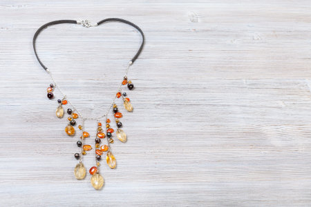 needlecraft background - top view of hand crafted necklace decorated by chains with natural citrine and cornelian gemstonesa and pearls red on gray wooden board with copyspaceの写真素材