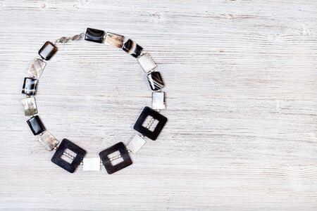 needlecraft background - top view of hand crafted necklace from horn frames, silver balls, square striped agate and nacre beads on gray wooden board with copyspaceの写真素材