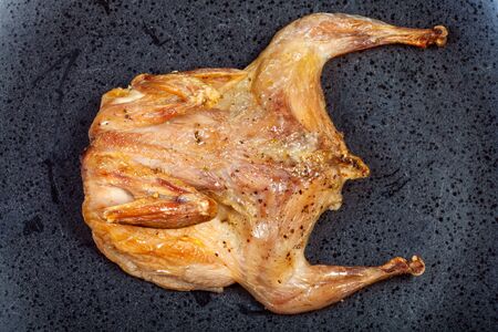 top view of roasted whole flattened quail on black plateの写真素材