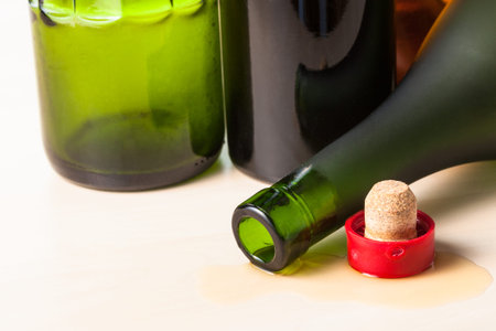 overturned brandy bottle and cork closeup near empty bottles on wooden boardの写真素材