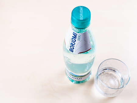 MOSCOW, RUSSIA - MAY 10, 2020: top view of plastic bottle of Borjomi and glass with water on light brown board. Borjomi is naturally carbonated mineral water from springs in Borjomi Gorge of Georgiaのeditorial素材