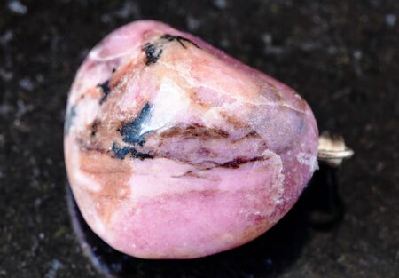 closeup of sample of natural mineral from geological collection - rolled Rhodonite rock on black granite background from Tajikistanの写真素材