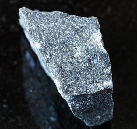 closeup of sample of natural mineral from geological collection - unpolished Andesite rock on black granite backgroundの写真素材