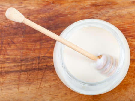top view of wooden stick in glass jar with natural organic white honey on wooden boardの写真素材