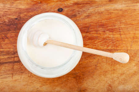top view of honey spoon in glass jar with natural organic white honey on wooden boardの写真素材