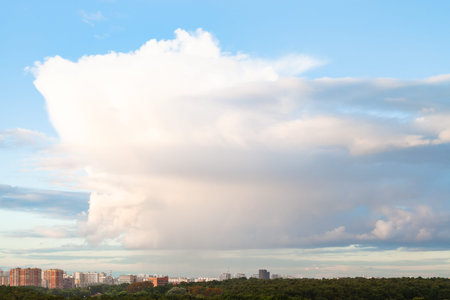 large cloud in blue sky over city and urban park in summer evening