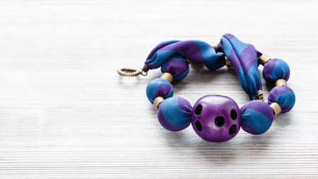 tangled handcrafted necklace of round beads wrapped in blue silk cloth and purple plastic ball with...