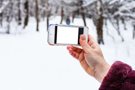female hand holds smartphone with cutout screen in snowy forest in winterの写真素材