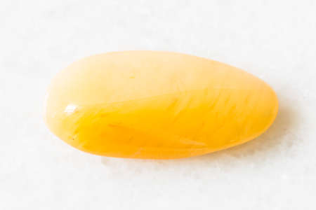 closeup of sample of natural mineral from geological collection - tumbled yellow chalcedony rock on white marble background from Indiaの写真素材
