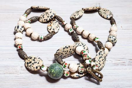 tangled handcrafted necklace from aplite cabochons, glass beads, green serpentinite ball, cracked cacholong beads and brass inserts on gray wooden table close upの写真素材