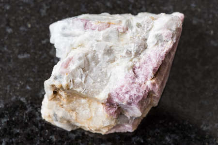 macro photography of sample of natural mineral from geological collection - raw pink Tourmaline mineral in feldspar and quartz rock from Kalba Range, Kazakhstan on black granite backgroundの写真素材