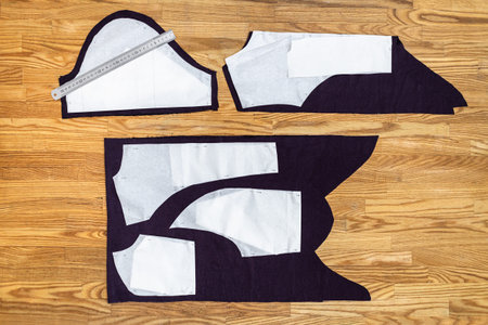 top view of paper layouts of sewing patterns of dress and steel ruler on purple fabric on wooden...