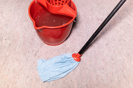 mop cleans linoleum flooring near red bucket with water at home