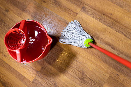 top view of rope mop cleans wooden laminate floor near bucket with water at homeの写真素材