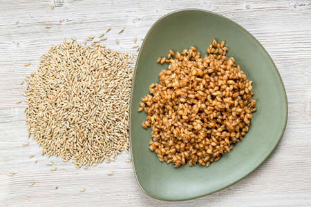top view of raw whole rye grains and boiled porridge on green plate on wooden tableの写真素材