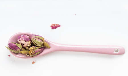 top view of old dried rosebuds in ceramic spoon on white plateの写真素材