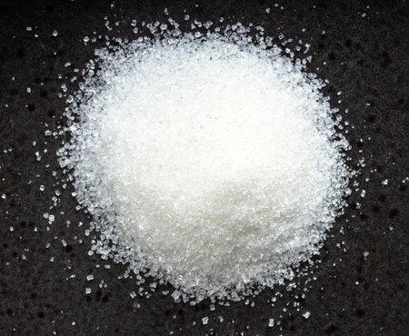 above view of pile of white refined beet sugar close up on black ceramic plate