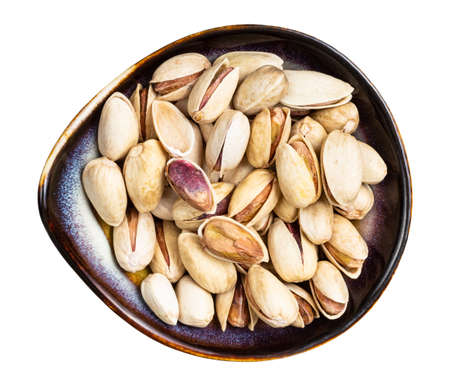 top view of shelled and ripe pistachio nuts in ceramic bowl isolated on white backgroundの写真素材
