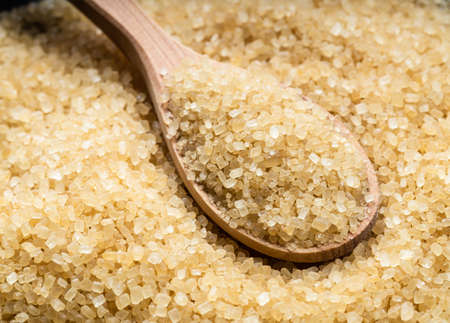 wooden spoon with demerara brown cane sugar close up on pile of sugarの写真素材
