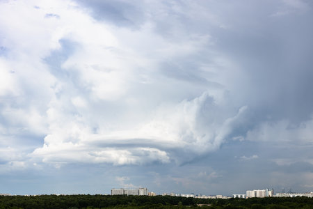 gray rainy clouds with whirls over city and forest on June dayの写真素材