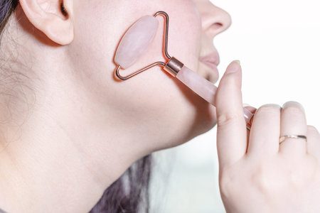 massaging cheek with quartz roller massager close up in technique of traditional chinese gua sha...