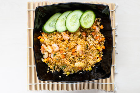 top view of portion of Com Rang Vietnamese wok fried rice with corn, peas, carrots, eggs, shrimp, squid in black bowl on wooden tableの写真素材