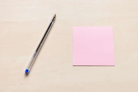 top view of blank pink sheet of note paper and blue pen on light brown wooden boardの写真素材