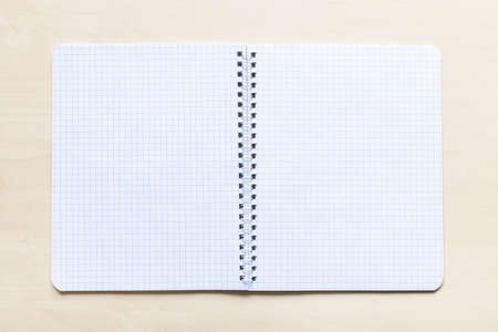 top view of open blank spiral notebook with squared pages on light brown wooden boardの写真素材