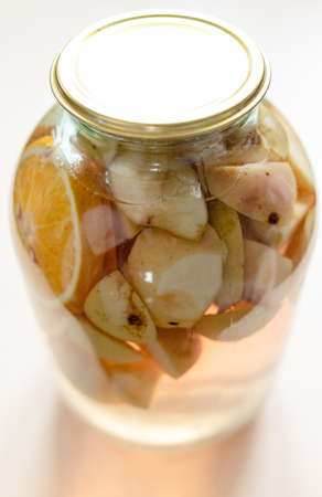3-liter glass jar with homemade compote (stewed fruit) made from sliced fresh apples and oranges close up on light brown tableの写真素材